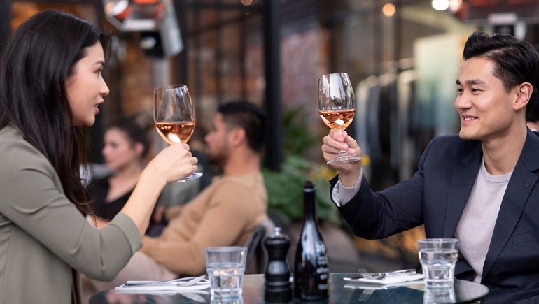 2 people at a bar holding wine glasses.